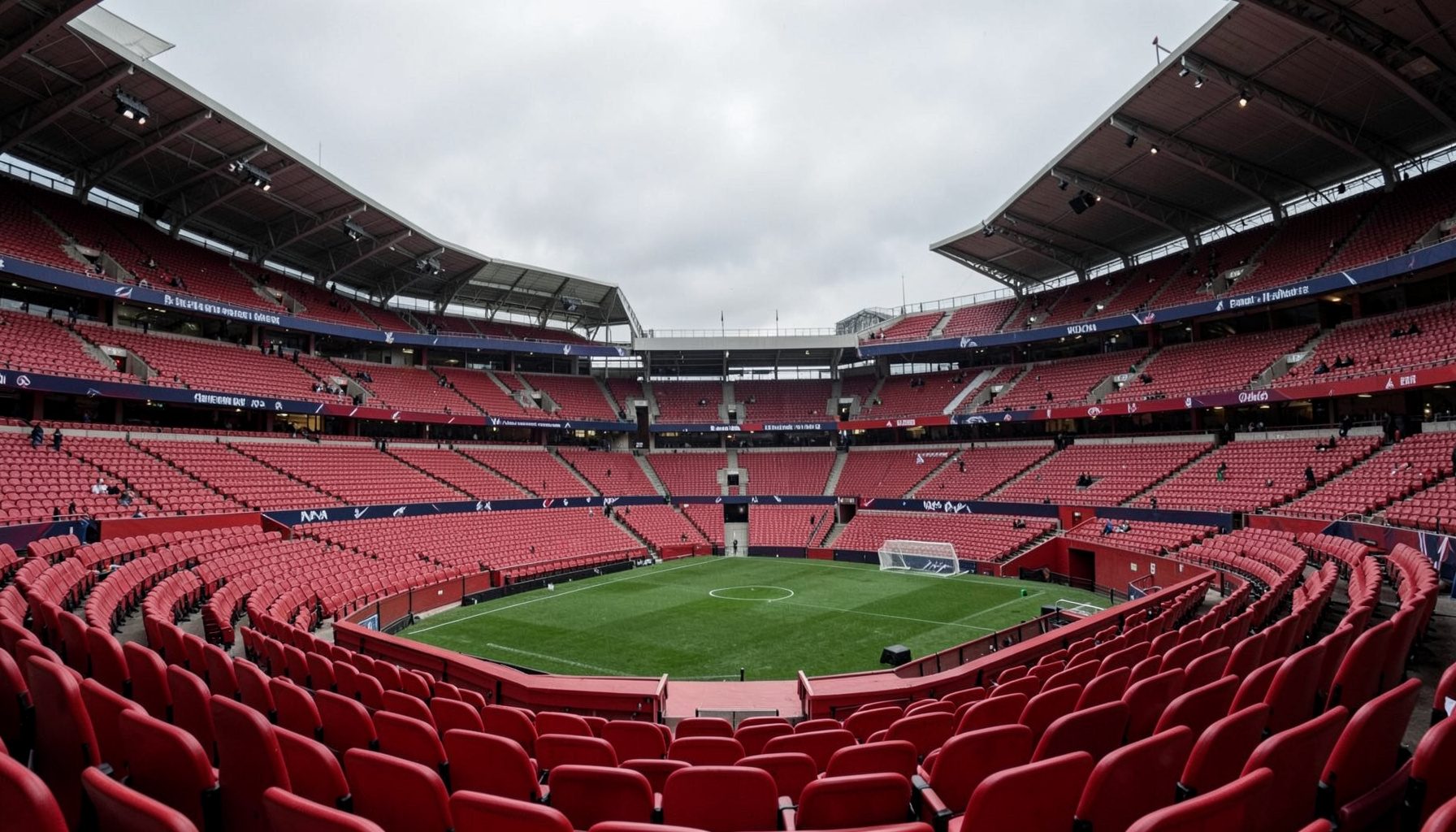 An empty dugout at a Premier League stadium, red seats under grey overcast sky, subdued and quiet atmosphere.